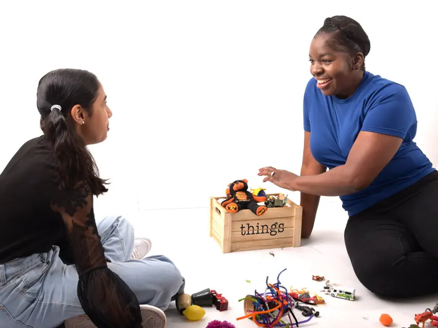 Judy Harrison sitting on the floor with a box of small figures and props, showing how a dramatherapy session can look
